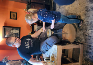 Dziewczynka wraz z Panem Garncarzem toczy naczynie z gliny.