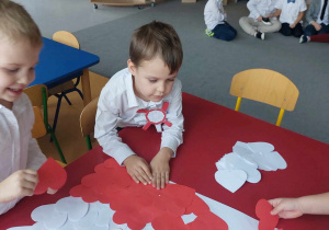 Dzieci wyklejają flagę białymi i czerwonymi sercami.