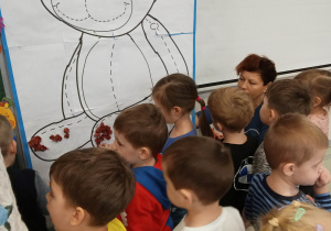 Przedszkolaki wyklejają misia bibułą.