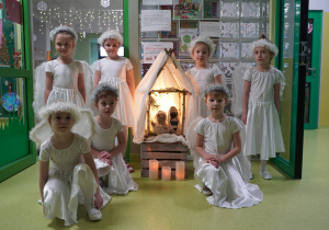 Dzieczynki przebrane za aniołki przy szopce wykonanej przez Panią Karolinę.