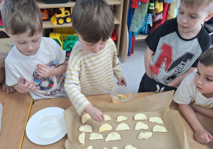 Chłopcy smarują ciasteczka jajkiem i posypują cukrem.