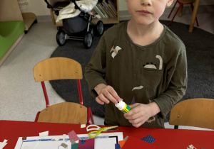 Chłopiec przykleja wycięte z kartonu elementy