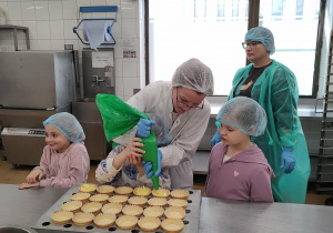 Dzieci obserwują, jak pani nakłada budyń na babeczki