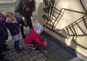dzieci ustawiają znicze pod pomnikiem